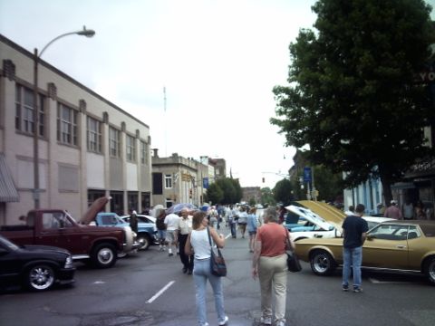 1995 Ford Probe - A street fair or car show is underway, with vehicles and pedestrians filling the roadway.