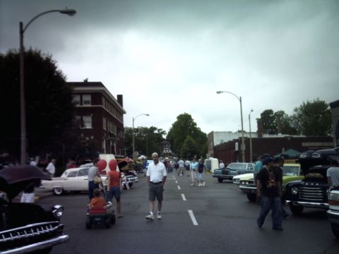 1995 Ford Probe - A street filled with cars and pedestrians during an outdoor event, with "SUPERMOTORS" branding at the bottom.