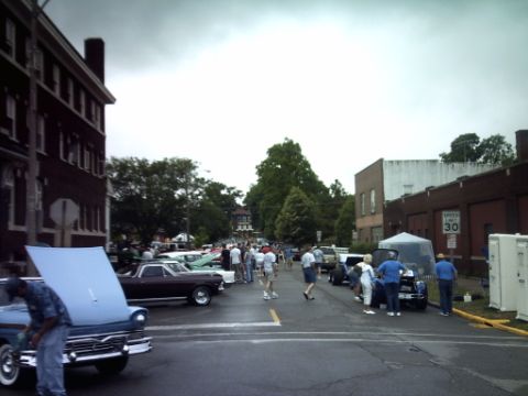 1995 Ford Probe - A car show is taking place on a street lined with buildings and trees.