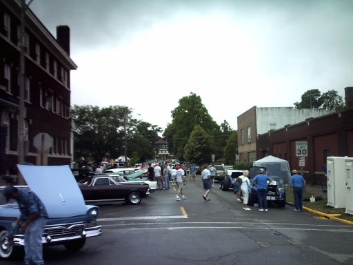 Street scene with classic cars parked and people milling around, some with hoods open
