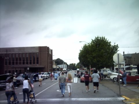 1995 Ford Probe - A street fair or car show is underway with many vehicles and pedestrians present.
