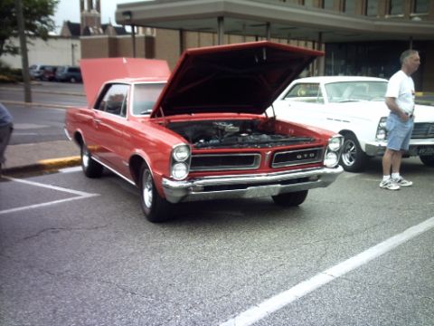 1995 Ford Probe - A red 1965 Pontiac GTO is parked with its hood open, alongside a white vehicle and a man.
