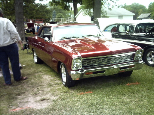 Red 1966 Chevrolet Nova parked on grass, front 3/4 view