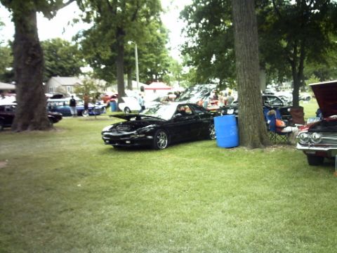 1995 Ford Probe - A black sports car is parked on a grassy field with its hood up, alongside other vehicles and people.