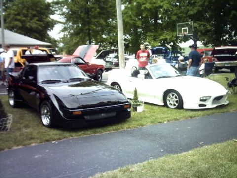 1995 Ford Probe - A black sports car is parked on the grass next to a white convertible.