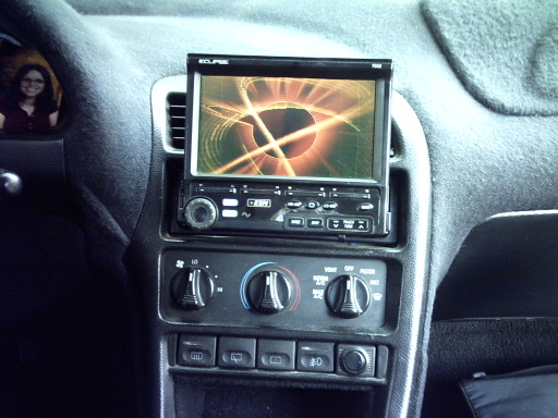Car interior showing dashboard with an aftermarket Eclipse stereo and climate controls. A person is reflected in the driver's side mirror