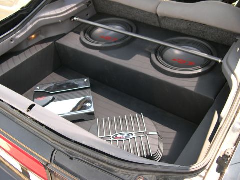 1997 Ford Probe - Custom stereo install in a hatchback cargo area: a black carpeted enclosure holds two down-firing subwoofers with red-logo dust caps, mount…