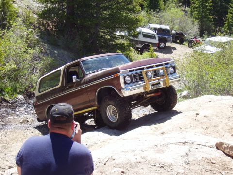 1979 Ford Bronco - A lifted SUV navigates a rocky trail, with other vehicles parked further up the path.