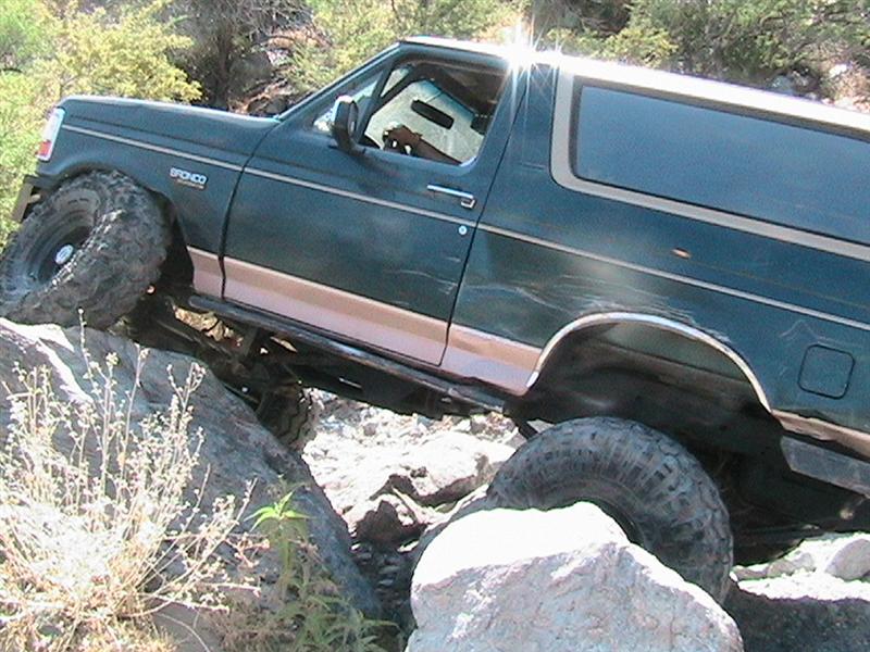 Green 1994 Ford Bronco with tan trim climbing over large rocks