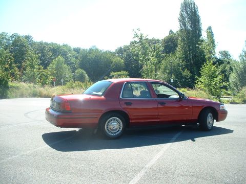 1999 Ford Crown Victoria - A red sedan is parked in an outdoor lot with trees in the background under a clear sky.