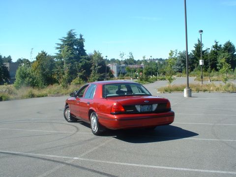 1999 Ford Crown Victoria - A red sedan is seen from the rear in a parking lot, with tire marks on the asphalt.