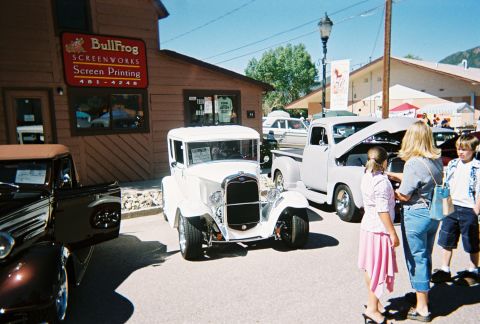 1972 Ford Ranchero - A car show features a white 1930s sedan and a pickup truck with its hood up.