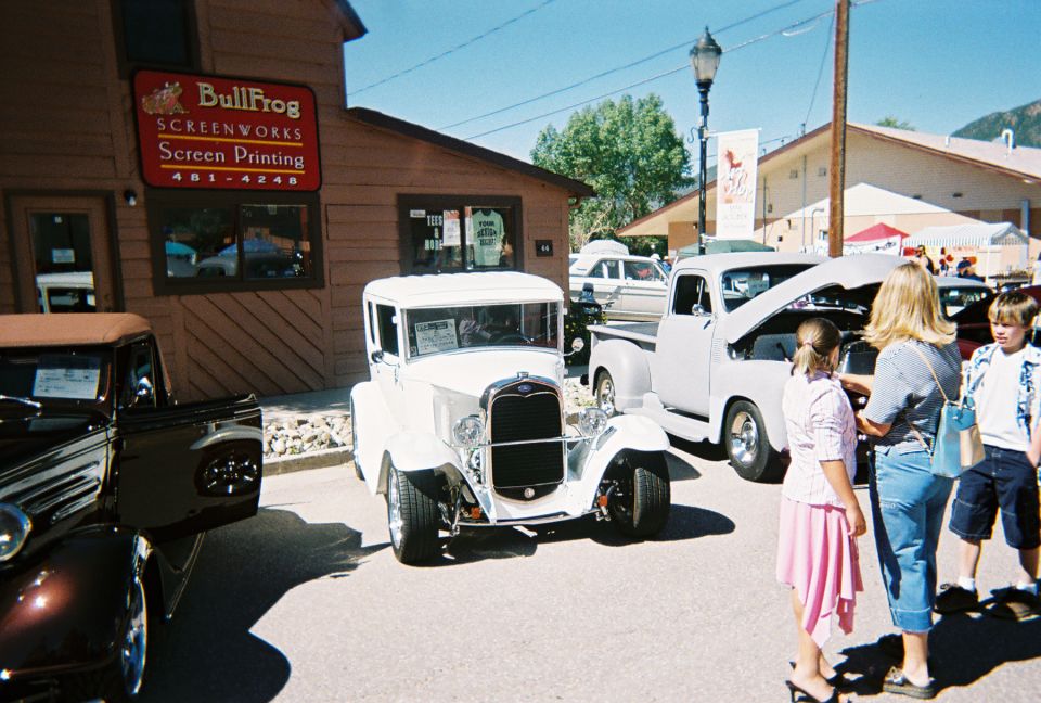 White 1930s sedan with black grille and chrome accents parked next to a light-colored pickup truck with hood open