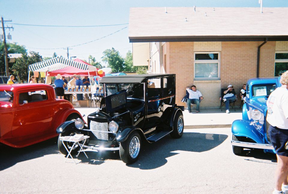 Black Model T hot rod between red and blue 1930s coupes at a street car show