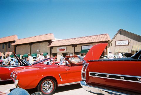 1972 Ford Ranchero - A red Ford Ranchero is parked at an outdoor car show with other vehicles and buildings in the background.