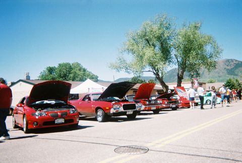 1972 Ford Ranchero - A line of cars, including a red 1972 Ford Ranchero with its hood open, are displayed at a car show on a sunny day.