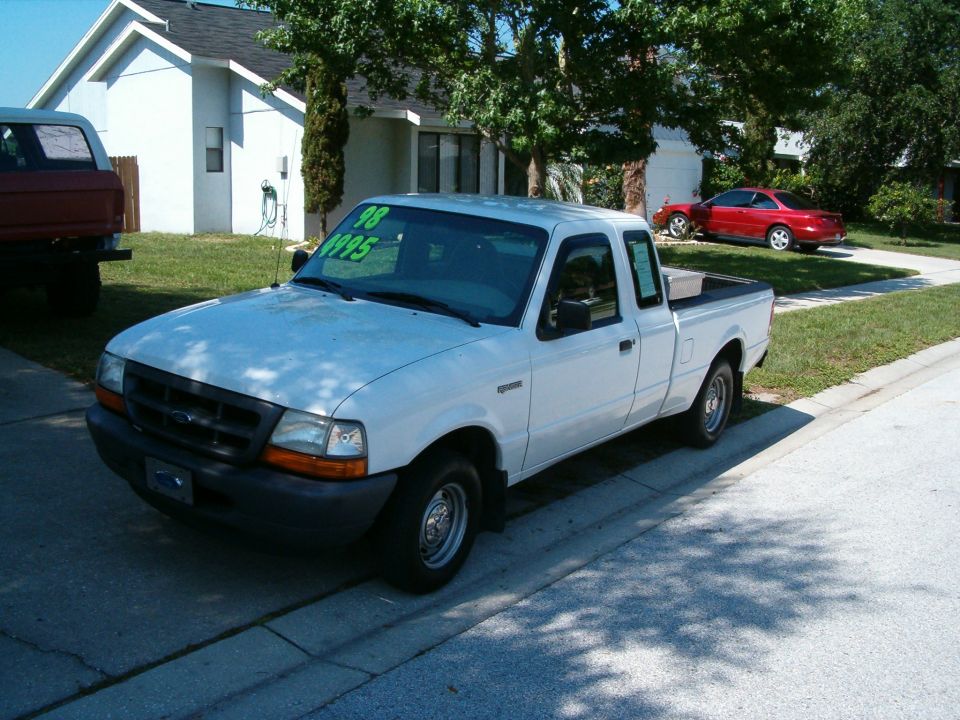 White Ford Ranger pickup truck parked on street, red car in driveway behind it