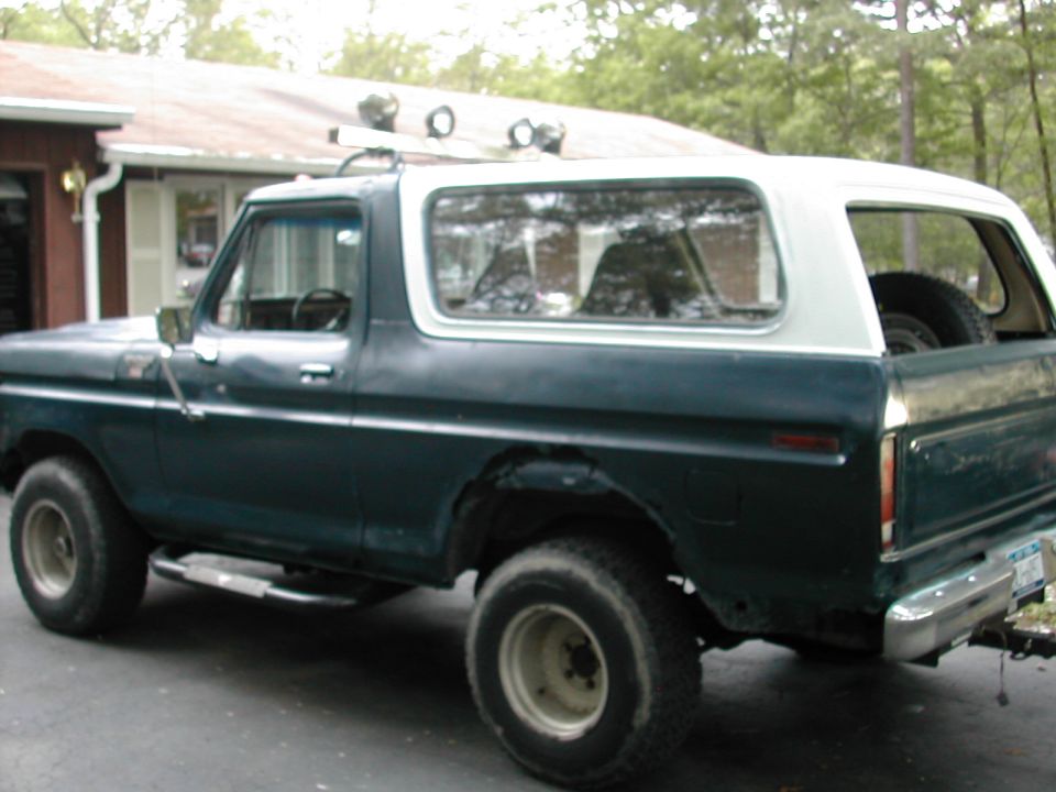 Side view of a dark green and white Ford Bronco with off-road lights on the roof rack