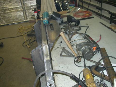 1995 Ford Bronco - A metal bumper part is on a workbench with tools, including a winch and an axe.