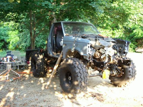 1985 Ford Bronco - This heavily modified truck, possibly a Ford Ranger or Bronco, sits in a yard with its front end severely damaged and large off-road tires…