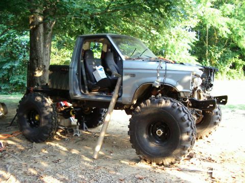1985 Ford Bronco - This heavily modified pickup truck sits on massive tires, with its front end partially disassembled.