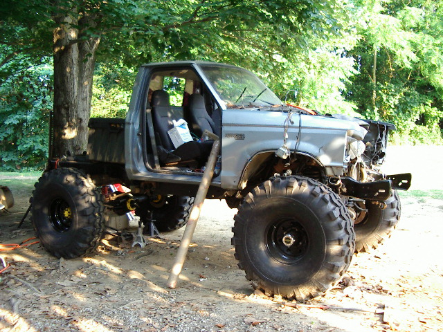 Modified pickup truck with oversized tires, missing front end components, and open doors