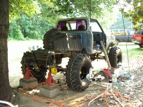1985 Ford Bronco - A heavily modified pickup truck is undergoing work outdoors, with tools and parts laid out nearby.