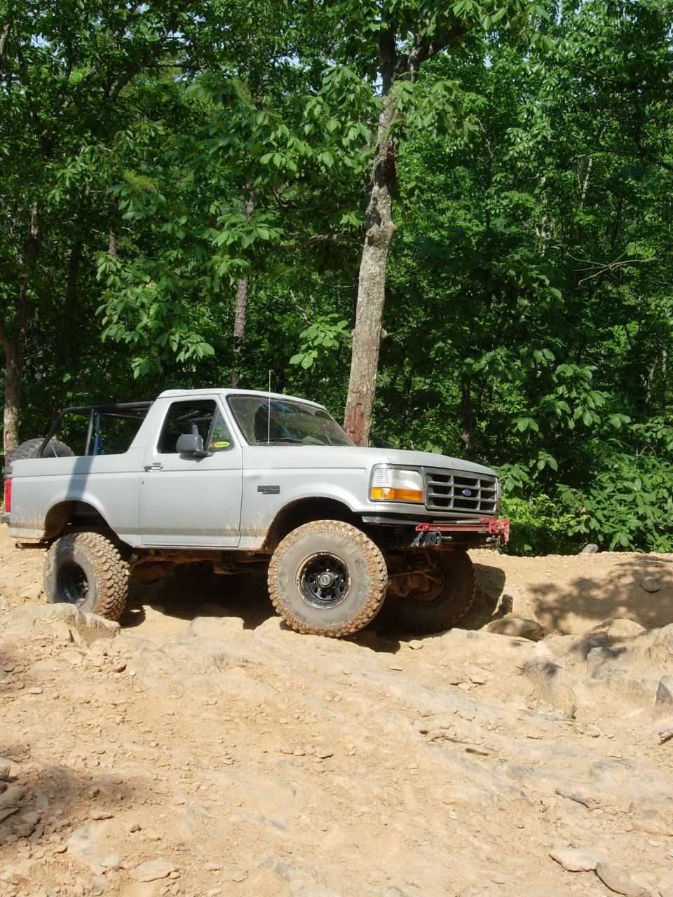 1995 Ford Bronco on a rocky dirt trail with trees in the background