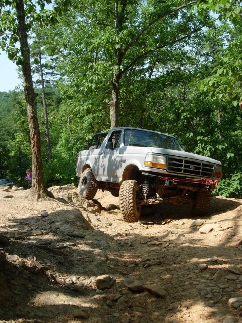 1995 Ford Bronco - A white Ford Bronco navigates a challenging off-road course with one wheel elevated.
