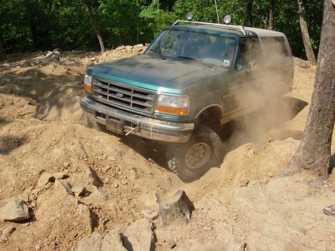1995 Ford Bronco - A green Ford Bronco tackles a challenging off-road course, kicking up dust.