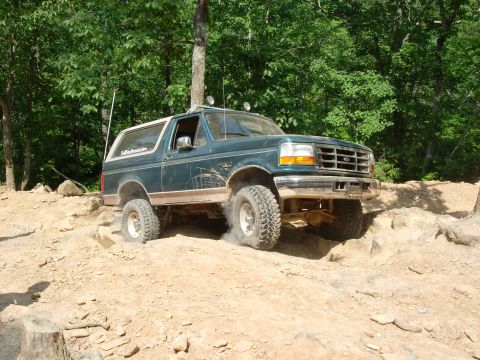 1995 Ford Bronco - A green 1995 Ford Bronco tackles an off-road trail with dust kicking up from its tires.