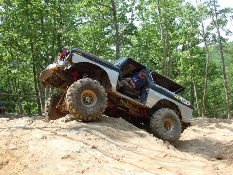 1995 Ford Bronco - Off-road Bronco navigating a steep, sandy incline with trees in the background.