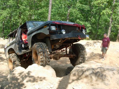 1995 Ford Bronco - A heavily modified black SUV with oversized tires is shown tackling a rocky off-road course.