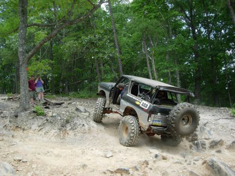 1995 Ford Bronco - An off-road vehicle navigates a challenging rocky trail in a wooded area.