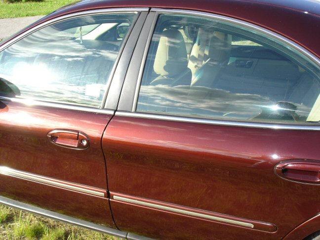 Side view of rear doors on a burgundy sedan with chrome window trim and tan interior visible