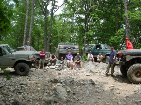 1995 Ford Bronco - Several off-road vehicles and their occupants pause on a rocky trail in a wooded area.