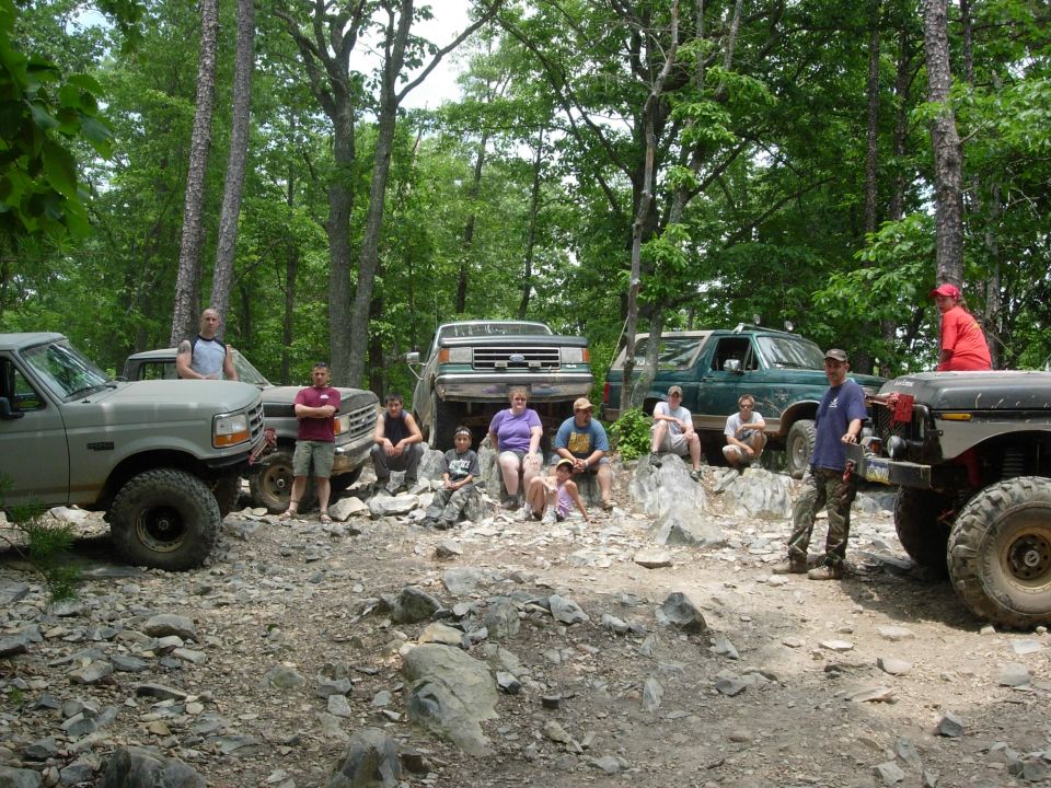 Group of off-road trucks and SUVs parked on a rocky trail, people gathered around