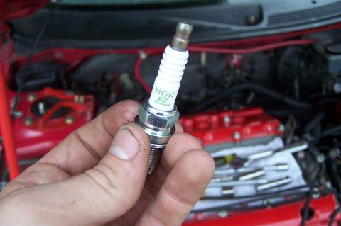 1997 Ford Probe - A hand holds a spark plug with the NGK R logo in front of a red engine bay.