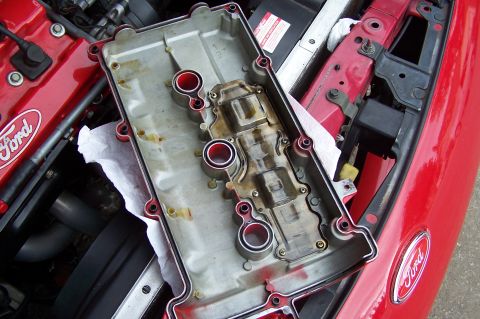 1997 Ford Probe - The removed valve cover shows internal engine components and oil residue, with a Ford logo visible on the engine block.