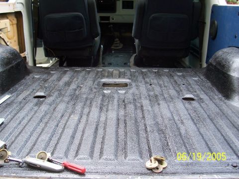 1979 Ford Bronco - The textured floor of a vehicle's interior is visible, with two dark seats and some tools in the foreground.