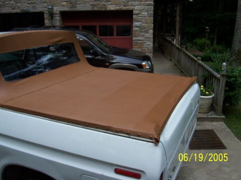 1979 Ford Bronco - A white pickup truck with a brown soft top is parked next to a black SUV in front of a garage.