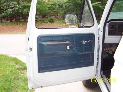 1979 Ford Bronco - Interior door panel of a white truck, showing blue upholstery and a chrome window crank, with a timestamp in the corner.