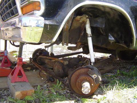 1979 Ford Bronco - Front axle and suspension components are disassembled from a black vehicle, resting on jack stands.
