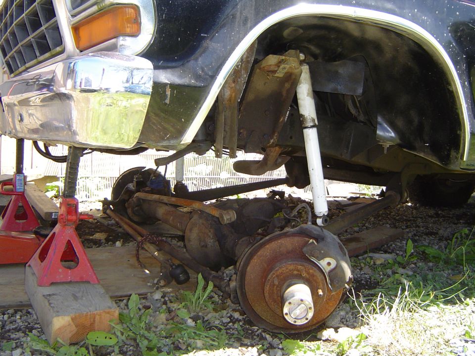 Front axle and suspension parts removed from a black vehicle, supported by red jack stands