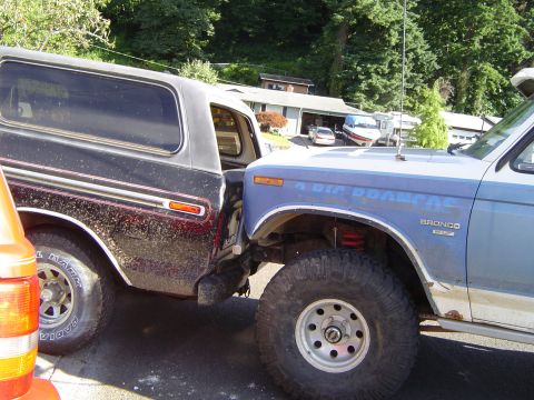 1979 Ford Bronco - A blue 1979 Ford Bronco is parked very close to a black SUV, with "4 BIG DOORS" visible on the fender.