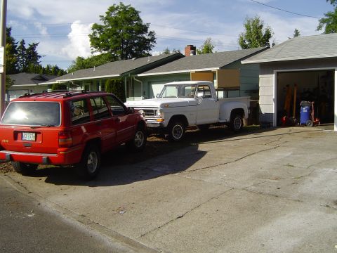 1979 Ford Bronco - A white 1973 Ford F-Series pickup truck is parked in a driveway next to a red Jeep Grand Cherokee, with a garage visible in the background.