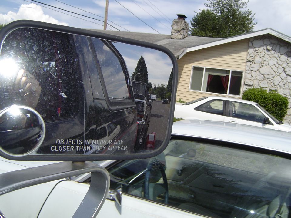 Reflection in side mirror shows a black SUV and a street scene. Text on mirror reads 'OBJECTS IN MIRROR ARE CLOSER THAN THEY APPEAR'