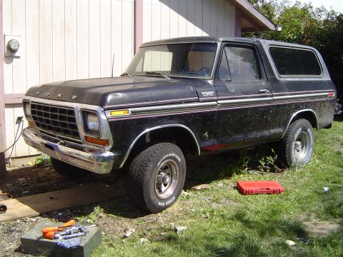 1979 Ford Bronco - This black 1979 Ford Bronco is parked on grass next to a building, with tools visible in the foreground.