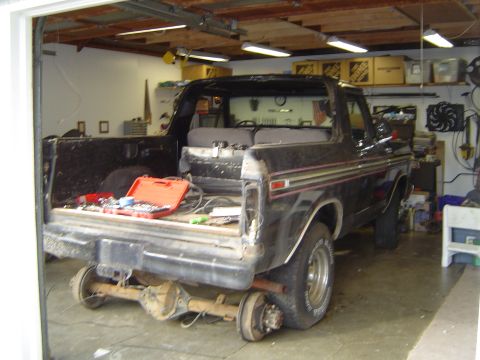1979 Ford Bronco - A black Ford Bronco is in a garage, with its rear axle detached and tools visible in the cargo area.