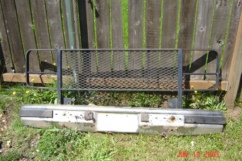 Black expanded-metal brush guard and white truck front bumper leaning on a wood fence